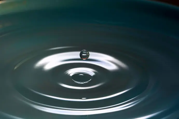 A drop of water above a rippling water.