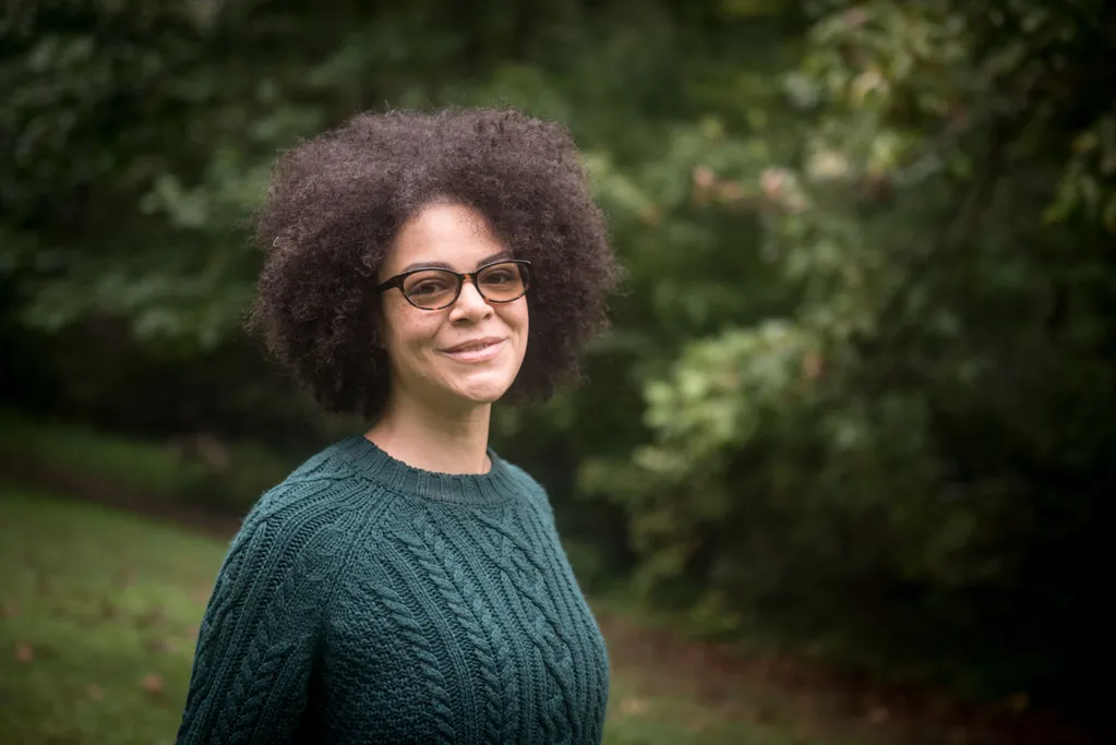 Christina Marrero, smiling, in a green sweaterin front of a blurred background of green foliage.